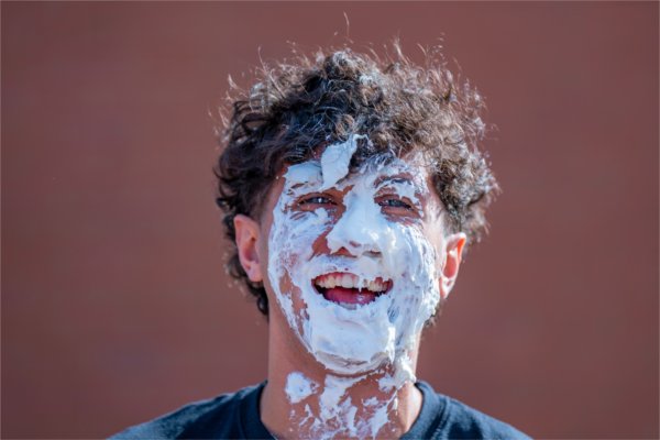 A college student laughs after having a pie thrown in their face. 