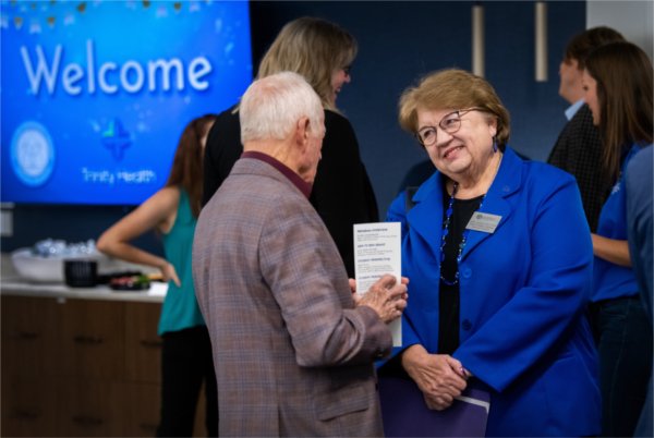 Linda Lewandowski, in blue blazer, smiling and talking with a man with gray hair, others in background at a reception