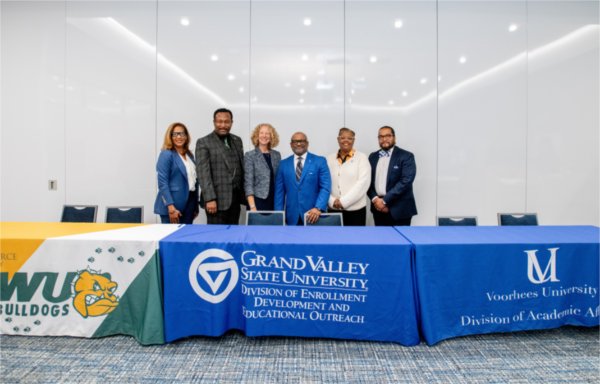 six people standing behind a table with banners from GVSU, Wilberforce and Voorhees universities