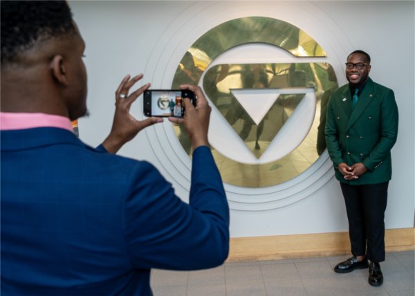 student taking a photo of another student who is standing by the gold GV