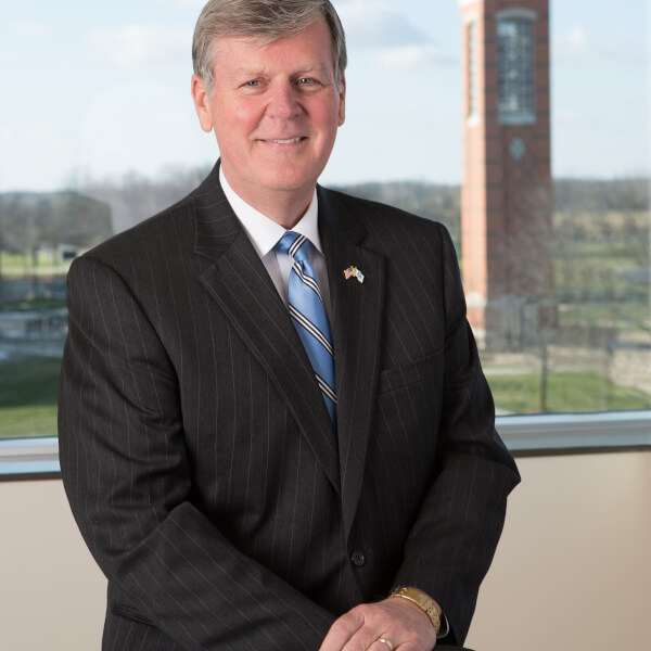 President Thomas J. Haas poses for a portrait. The campus clock tower is in the distant background.