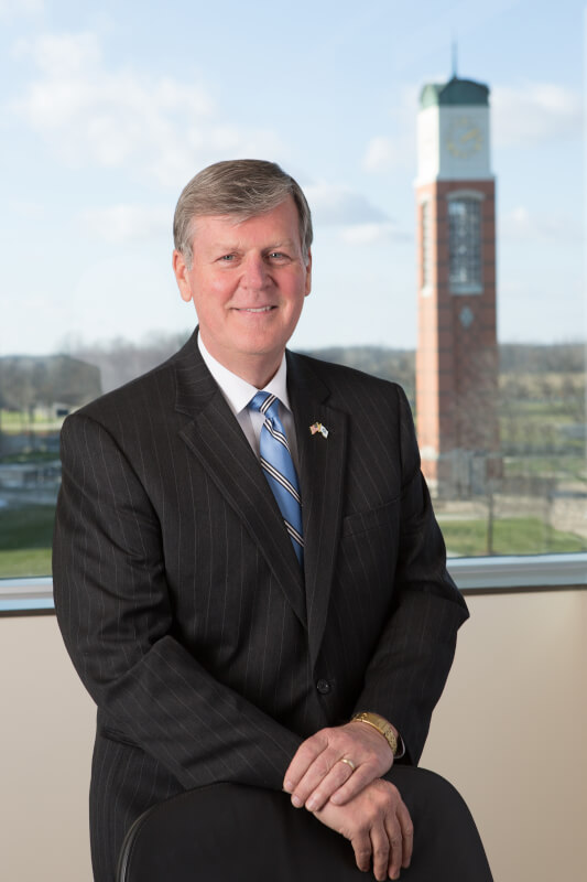 President Thomas J. Haas poses for a portrait. The campus clock tower is in the distant background.