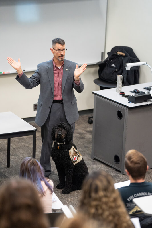 man at front of classroom, service dog at his feet