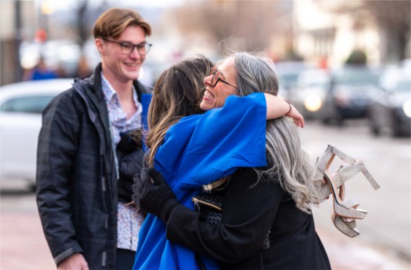  A graduate holding high heels hugs a person.