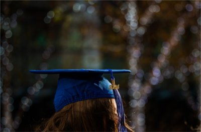 Holiday lights twinkle behind a person wearing a blue mortar board cap and 2024 tassel.