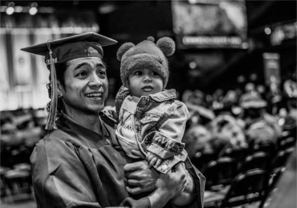  A dad wearing a cap and gown holds his young infant son. 