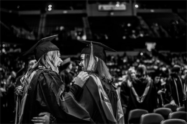  Two graduates laugh as they put their arms around each other. 