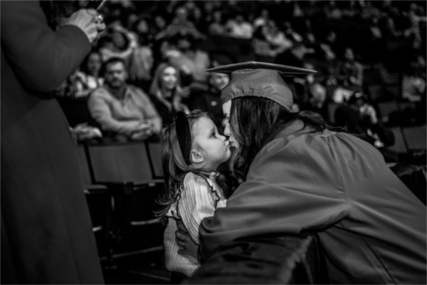  A mother in cap and gown kisses her young daughter. 