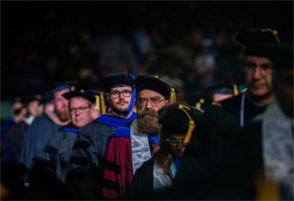  A group of faculty in regalia process into a commencement ceremony.