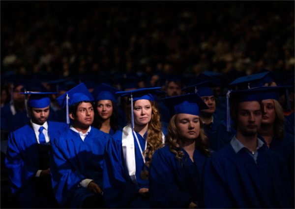  A group of graduates in blue caps and gowns listen to the speaker. 