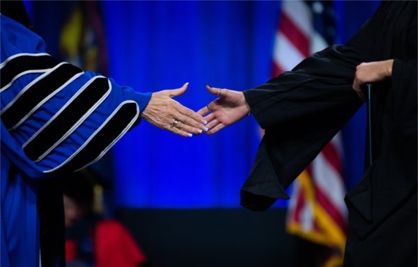  A university president stretches out her hand to shake the hand of a graduate. 