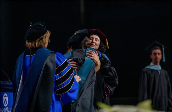 A graduate hugs a person on stage after being hooded.  