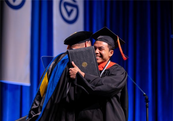   A graduate reacts to receiving their diploma with a hug.