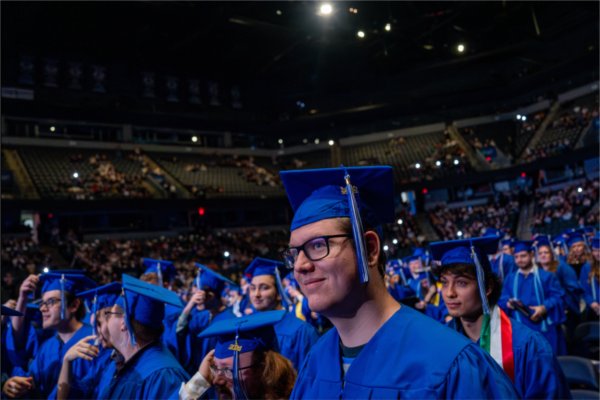   Graduates smile while wearing blue caps and gowns during the end of a commencement ceremony.