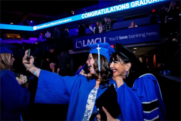  A person wearing a blue cap and gown poses with a selfie with the university president.