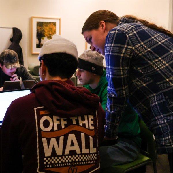 three people looking at a laptop, two seated, one standing