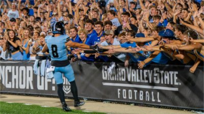 Grand Valley football player celebrates with students after scoring a touchdown.