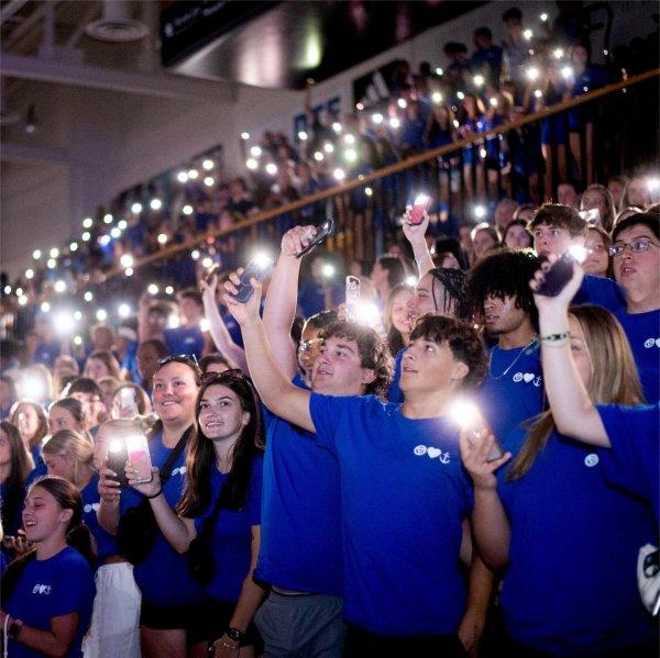 students in blue tshirts standing holding cell phones with lights on