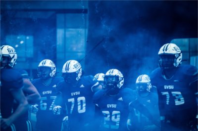 GVSU football players run on to the Lubbers Stadium field through a cloud of blue smoke.