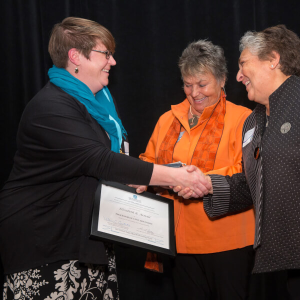 Three women on stage, one with certificate and shaking hands