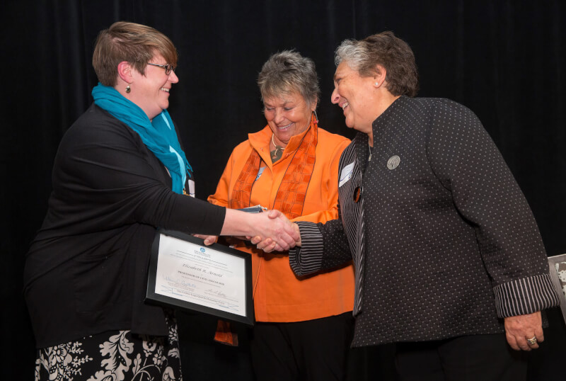 Three women on stage, one with certificate and shaking hands