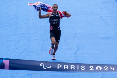 Chris Hammer carries the U.S. flag as he crosses the finish line for his Para Triathlon event at the 2024 Paris Paralympic Games.