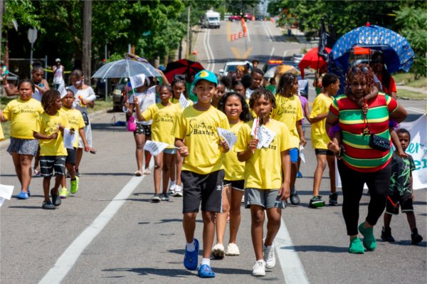A group of kids in yellow shirts that read &ldquo;Summer Baxter&rdquo; walk in a parade.