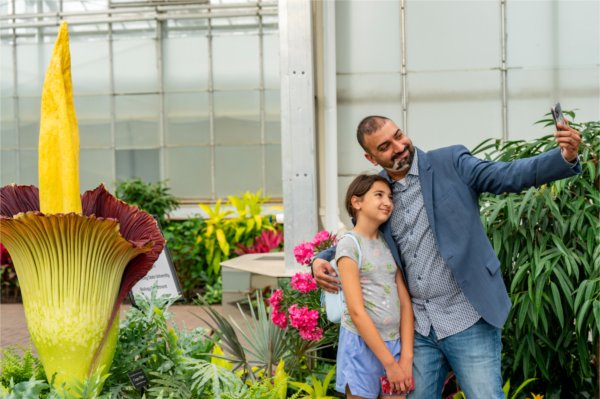 Two people smile while taking a selfie. The corpse flower is in the background.