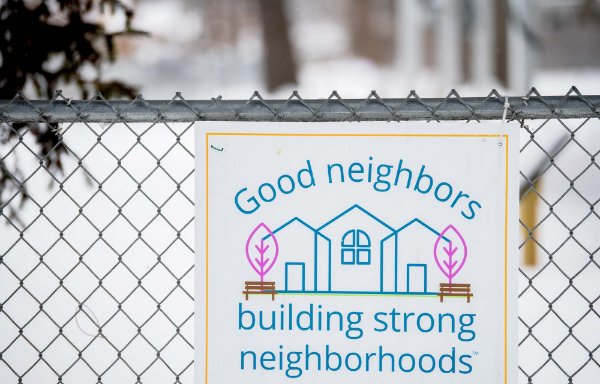 A sign on a fence says in blue writing, "Good neighbors building strong neighborhoods." There also are drawn images of homes.